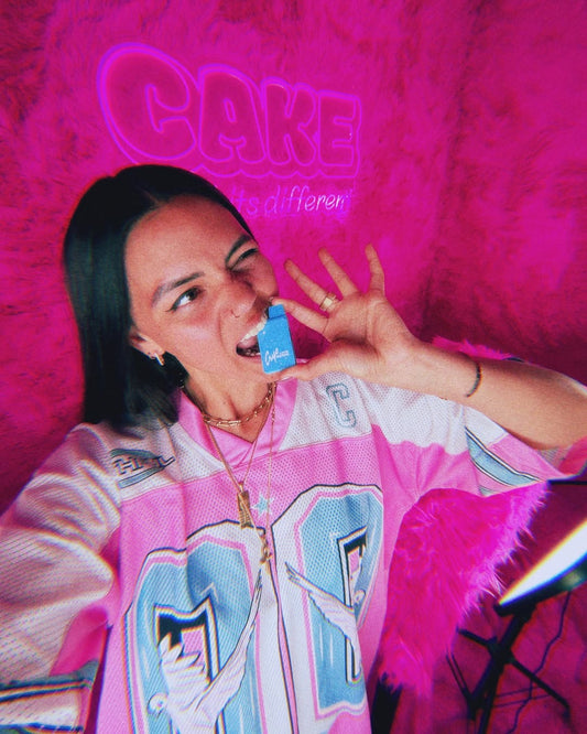 Person holding Cake Designer Distillate against bright pink backdrop highlighting low-temp dab flavor experience.